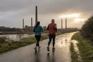 two runners run along a cycle path with industrial background.